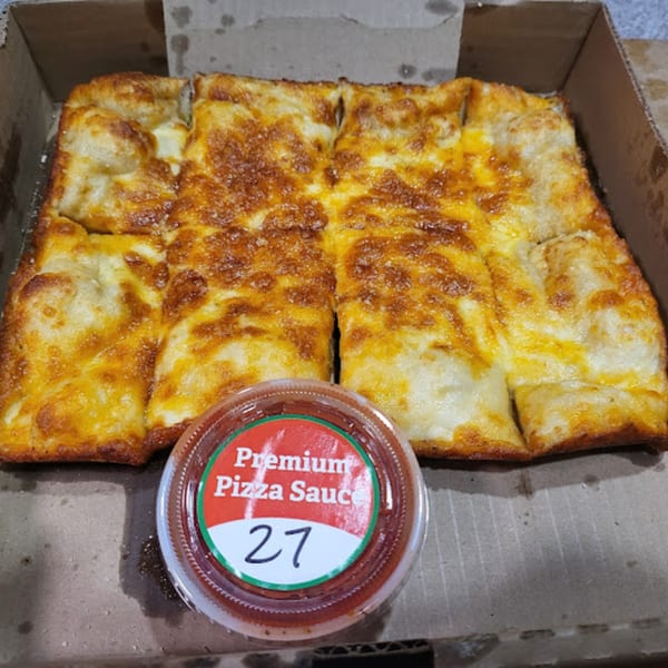 Cheesy breadsticks with a side of Karl's Place Premium Pizza Sauce in a cardboard box.