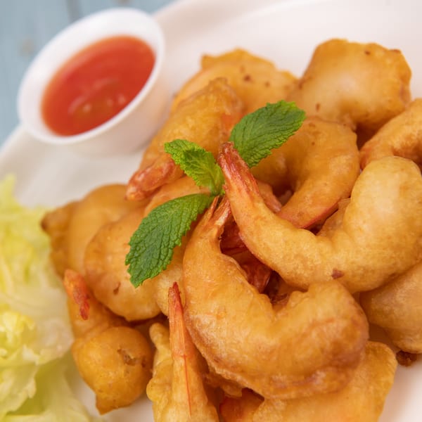 Golden-fried shrimp with a sprig of mint, lettuce, and a side of red dipping sauce.