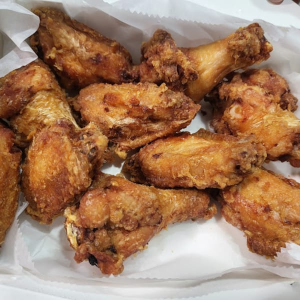 A close-up of several crispy, golden-brown fried chicken wings in a white paper-lined container.